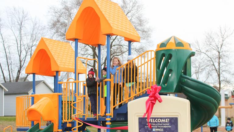 a group of happy elementary school children on new playground equipment purchased for a city park off of a Sourcewell awarded contract