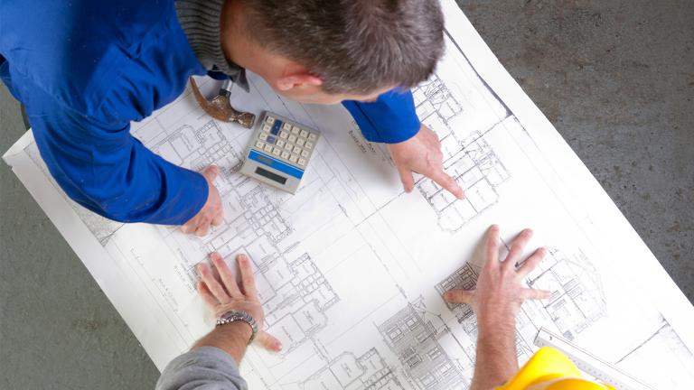Two men leaning over a table reviewing a detailed building plan