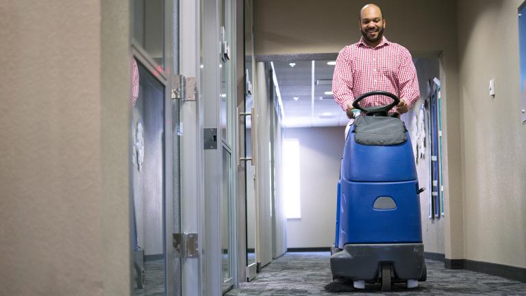 a smiling man on a ride on vaccuum cleaning the hall of an office building